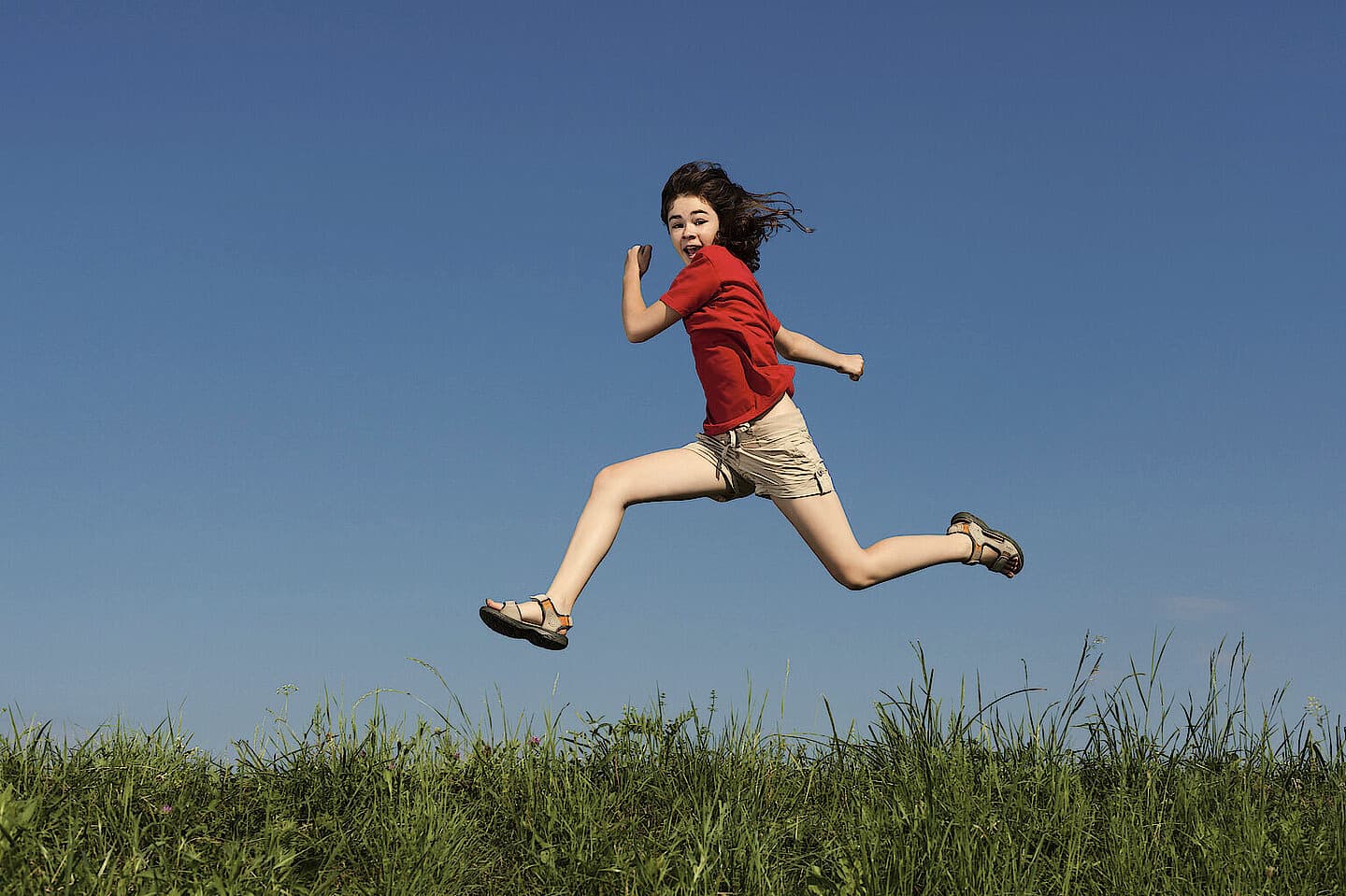 A girl leaping across a meadow under a blue sky
